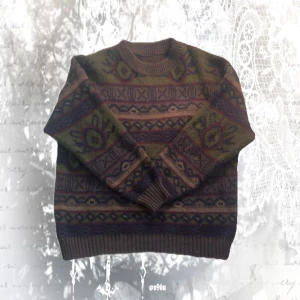 Mönstrad stickad tröja i jordnära färger - Säljer en mysig stickad tröja med unikt mönster i grönt, brunt, lila och beige. Tröjan har rund hals, ribbade muddar och långärmade. Perfekt för dig som gillar retrovibbar och vill ha något som sticker ut i garderoben.