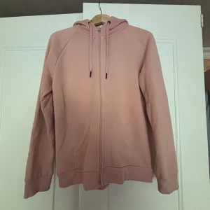 Huvtröja från Peak Performance - Säljer en rosa hoodie från Peak Performance med dragkedja och huva. Tröjan har snörning i huvan, fickor framtill och ett coolt kamouflagemönstrat tryck på ryggen. Perfekt för chill dagar eller när du vill ha en avslappnad stil. Skriv vid frågor🤩