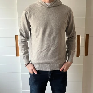 Beige hoodie från Oscar Jacobson - Säljer en stilren beige hoodie från Oscar Jacobson i storlek M. Tröjan är tillverkad i Italien och har en klassisk design med långa ärmar och ribbade muddar. Perfekt för en avslappnad och elegant look.