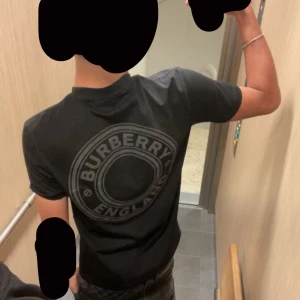 Svart t-shirt från Burberry - Snygg svart t-shirt från Burberry med ett stort tryck på ryggen och litet på framsidan, Perfekt för en stilren look. T-shirten har korta ärmar och en klassisk passform.