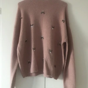 Rosa tröja med pärldetaljer från H&M - Säljer en mjuk rosa tröja från H&M med dekorativa pärldetaljer på framsidan. Tröjan har långa ärmar och en rund halsringning. Perfekt för en stilren och bekväm look.
