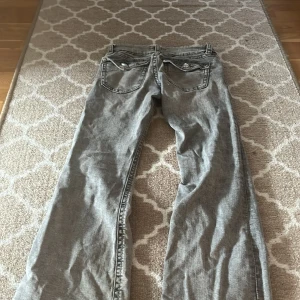 Grå jeans från Gina Tricot - Säljer ett par grå jeans från Gina Tricot. De har en klassisk design med knapp och dragkedja framtill. Perfekta för en avslappnad stil.