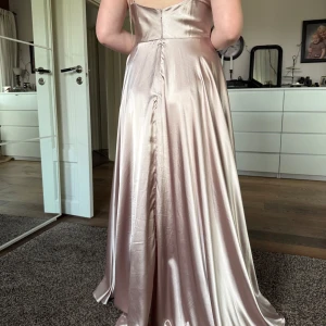 Champagnefärgad/rosa balklänning - Säljer min balklänning i satin. Bilderna är tyvärr några år gamla och då klänningen inte längre passar mig har jag valt att inte ta några nya, tar gärna fler vid önskemål. Klänningen har justerbara smala axelband som man knyter och är insydd i midjan. Klänningen satt perfekt med klackskor på mig som är 170 cm💕klänningen är från Helenas Boutique i Malmö och i storlek L, men insydd på några ställen.  Endast använd en gång💕