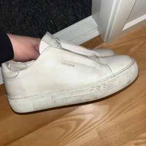 Vita sneakers från Axel Arigato - Säljer ett par stilrena vita sneakers från Axel Arigato. Skorna har en minimalistisk design med diskret logga i guld på sidan. Perfekta för en casual look.