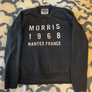 Mörkblå tröja från Morris - Säljer en mörkblå tröja från Morris med texten 'Morris 1968 Nantes France' i vitt på framsidan. Tröjan har långa ärmar och ribbstickade muddar vid ärmslut och nederkant. Perfekt för en avslappnad stil.