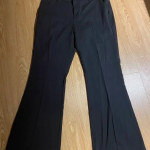 Svarta kostymbyxor - Snygga svarta kostymbyxor med hög midja och rak passform. Perfekta för en stilren look. Byxorna har hällor för bälte och pressveck framtill.