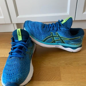 Blå löparskor från Asics - Snygga blå löparskor från Asics med gröna detaljer och snörning. Skorna har en ventilerande ovandel och en slitstark sula för bra grepp. Perfekta för löpning och träning.