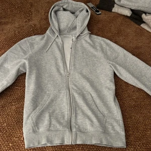 Weekday Grå hoodie med dragkedja - Säljer en stilren grå hoodie med dragkedja och fickor framtill. Perfekt för en avslappnad look. Den har en bekväm passform och är i mjukt material. Tröjan är från weekday nypris cirka 500 