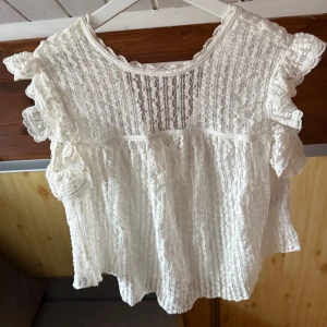 Vit spetsblus  - Säljer en söt vit spetsblus från Nelly med volangdetaljer och korta ärmar, använd en gång 