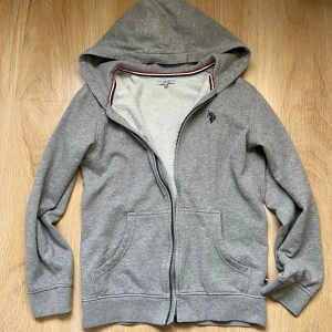US POLO ASSN hoodie - Säljer denna gråa zip up hoodien från US POLO ASSN. Köpt här på Plick och använd två gånger av mig. Säljer då den är lite för liten för mig. Bra skick och inga defekter 💕
