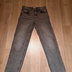 Grå jeansbyxor - Snygga grå jeansbyxor med klassisk femficksdesign. De har en rak passform och är perfekta för en avslappnad stil. Byxorna har en knapp och dragkedja framtill.