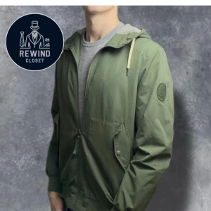 Grön vindjacka från Jack & Jones - Säljer en stilren grön vindjacka från Jack & Jones. Jackan har dragkedja framtill, huva med snörning och praktiska fickor med knappar. Perfekt för vår och höst!