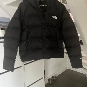 Svart dunjacka med huva från The North Face - Svart The North Face jacka, har ett lagat hål på höger arm men inget man märker när jackan sitter på. Köpt från The Norh Face hemsida Nypris: 2899kr Mitt pris: 1000kr