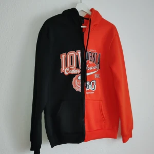 Svart och orange hoodie från Romwe - Cool hoodie från Romwe i en unik design med ena halvan svart och andra halvan orange. Den har en stor ficka framtill och tryck med text på bröstet. Perfekt för en avslappnad stil.