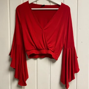 Röd omlottopp med volangärmar - Snygg röd omlottopp med långa volangärmar. Toppen har en v-ringad design och är croppad med elastisk midja.❤️