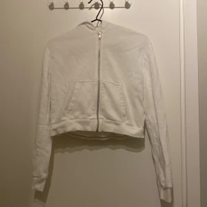 Vit croppad hoodie från H&M 🩷 - Säljer en vit croppad hoodie från H&M med dragkedja framtill och en praktisk huva. Den har långa ärmar och en bekväm passform. Perfekt för både hemma mys och till vardags! Har inte fläckar/lagningar/hål och är från HM i storlek 158-164! 🩷 Pris kan diskuteras vid snabbt köp och skriv för fler bilder! 🩷