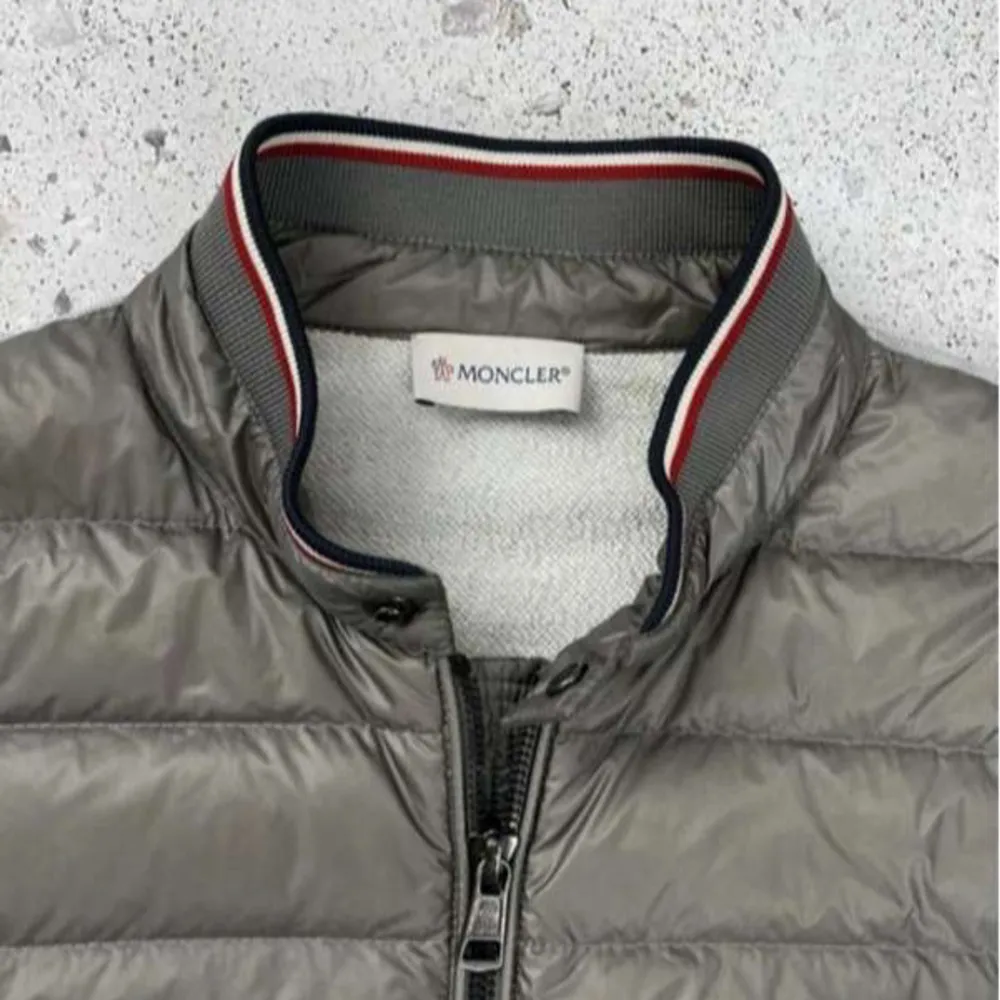 Säljer en stilren grå pufferjacka från Moncler med dragkedja och ribbad krage. Jackan har långa ärmar i en kontrasterande grå nyans och Moncler-logga på ärmen. Perfekt för kyligare dagar.. Takit.
