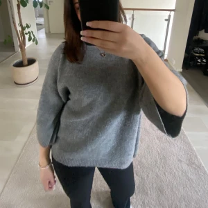 Grå stickad tröja - Säljer en mysig grå stickad tröja med trekvartsärmar. Perfekt för kyliga dagar och enkel att matcha med olika outfits. Tröjan har en avslappnad passform och är superbekväm att bära.