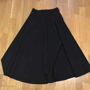 Svart långkjol - Elegant svart långkjol med ett flödande fall. Perfekt för en stilren look. Kjolen har en enkel design som gör den lätt att matcha med olika toppar.