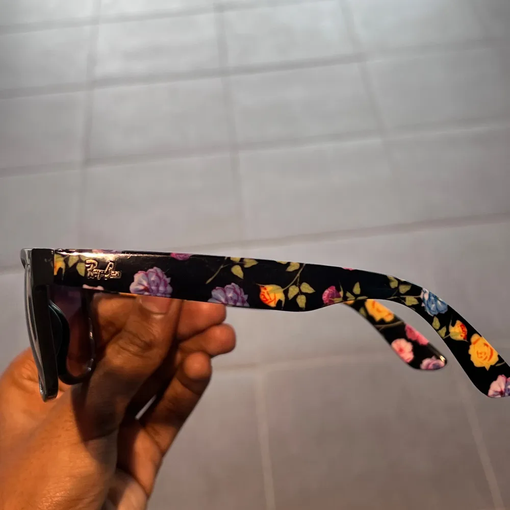 Snygga svarta solglasögon från Ray-Ban med ett coolt blommigt mönster på skalmarna. Perfekta för att ge en touch av stil till din look. Tillverkade i Italien med hög kvalitet.. Asusteet.
