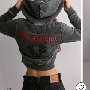 Grå hoodie från True Religion - Snygg grå hoodie från True Religion med röd logga på bröstet och ryggen. Jackan har dragkedja och en skön huva. Perfekt för en avslappnad stil. Nypris 1199:-