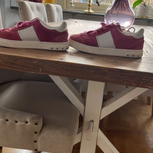 Rosa och vita sneakers med nitar - Snygga röd/rosa sneakers med vita detaljer och coola nitar på sulan. Skorna har snörning och en stilren design som passar perfekt för en trendig look. Från märket valentino i storlek 38/39 tar även byten.