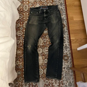 Levi's jeans med slitna detaljer - Säljer ett par Levi's jeans i mörk tvätt med slitna detaljer på knäet. Klassisk femficksdesign med knappgylf och bälteshällor. Perfekta för en avslappnad stil. Som ni ser så är passformen slim/straight. Jeansen är 101 cm långa och midjan är från sida till sida 41 cm. Hör av er om ni vill fråga något