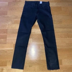 Svarta Jeans/Chinos - Snygga mörkblå/svarta chinos med en klassisk design. De har en rak passform (Slim Fit) och är perfekta för en stilren look. Byxorna har knappar och dragkedja framtill. Tunna Jeans. Mått från Gren till ben slut 74cm