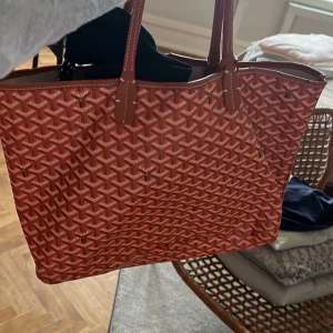 fin väska - Snygg röd shoppingväska med ett unikt mönster. Väskan har två handtag och är perfekt för att bära med sig allt man behöver. Den är både stilren och praktisk.