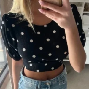Svart prickig croppad topp - Säljer en svart croppad topp med vita prickar. Toppen har korta ärmar och en knytning i ryggen som ger en snygg detalj. Perfekt för en trendig look!🫶🏽