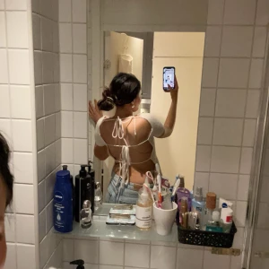 Vit kortärmad topp med snörning - Säljer en vit kortärmad topp med öppen rygg och snörning. Toppen har en unik design med knytband som ger en trendig look. Perfekt för att styla med jeans eller kjol.