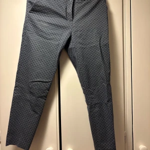 Mönstrade kostymbyxor från H&M - Säljer ett par mörkblå kostymbyxor från H&M med vitt geometriskt mönster. Byxorna har normal passform och är perfekta för dig som vill ha en stilren men ändå unik look. Materialet känns mjukt och bekvämt.