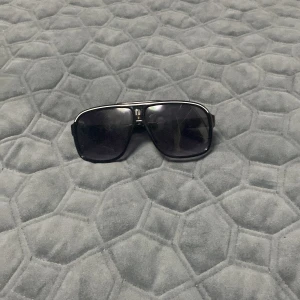 Svarta solglasögon med bred båge - Snygga svarta solglasögon med bred båge och mörka glas. Klassisk och sportig design med markerad ram och raka skalmar. Perfekta för att ge en cool look och skydda ögonen mot solen.