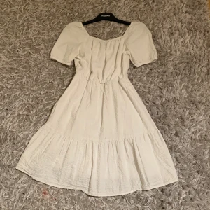 Vit klänning med puffärmar och öppen rygg - Superfin vit klänning från Kappahl med puffärmar och snygg öppen rygg med knytning. Klänningen har en lätt rynkad kjol och fyrkantig ringning framtill. Perfekt för sommarens alla tillfällen!