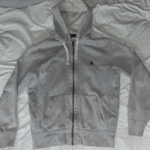 Grå zip hoodie   Ralph Lauren - Säljer en ljusgrå zip hoodie från Polo Ralph Lauren i S med dragkedja och huva.  Finns få små defekter vid ärmslutet men i helhet mycket bra skick.