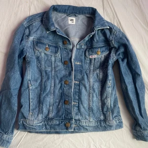 Blå jeansjacka från Lee x H&M - Säljer en klassisk blå jeansjacka från Lee x H&M. Jackan har knappar framtill, två bröstfickor med lock och knapp samt en snygg krage. Perfekt för dig som gillar en tidlös och avslappnad stil.