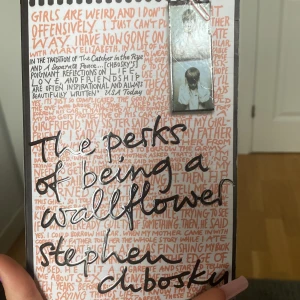 The Perks of Being a Wallflower - En engelskspråkig roman av Stephen Chbosky. Omslaget är vitt med handskriven text i orange och svart, samt ett foto av en pojke. Boken är i pocketformat och handlar om tonårsliv, vänskap och att växa upp.