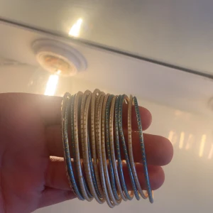 Guld- och turkosfärgade armband - Flera tunna armband i guld med turkosa detaljer. Armbanden har en glittrig yta och passar perfekt som accessoar för att ge lite extra färg till din outfit.
