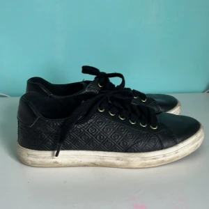 Svarta sneakers från Gant med mönster - Svarta sneakers från Gant med snyggt präglat mönster på sidorna och guldfärgade detaljer. Skorna har svarta snören, vit sula och Gant-logga baktill. Perfekta för en stilren och avslappnad look.