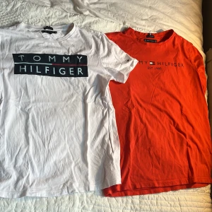 Två t-shirts från Tommy Hilfiger - Säljer två snygga t-shirts från Tommy Hilfiger i ekologisk bomull. En är vit med stor logga framtill och en är röd med diskret tryck. Båda har rund hals och korta ärmar. Perfekta för en clean och stilren look.