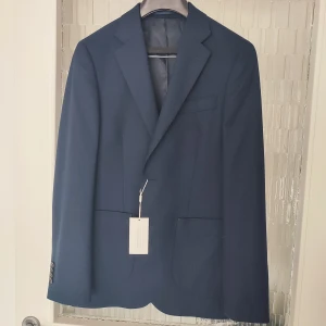 Mörkblå kavaj från These Glory Days i storlek 44 - Mörkblå kavaj från These Glory Days. Storlek 44. Modellen på kavajen heter T Vince Patch Blazer 593 Dark Navy. Kavajen är helt ny med alla lappar kvar! Nypris på denna är 1999kr. Köpt på herr-avdelningen men funkar lika bra på en kvinna. Om du vill köpa kavajen så kan jag naturligtvis skicka dig fler bilder.