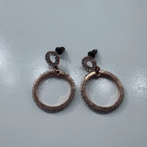 Runda örhängen i roséguld - Säljer ett par snygga örhängen i roséguld med två cirklar, där den mindre cirkeln är dekorerad med glittriga stenar. Perfekta för att lyfta din look med lite extra bling!