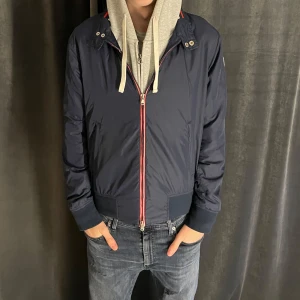 Mörkblå bomberjacka från East West - Säljer en mörkblå bomberjacka från East West med röda och vita detaljer vid dragkedjan. Perfekt för dig som gillar stilren och sportig look. Skick 8/10✅ Pris kan diskuteras vid snabb affär💸