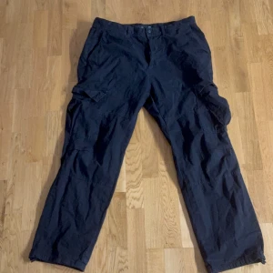 Svarta cargobyxor från Bershka - Svarta cargobyxor från Bershka med flera fickor på sidorna. Byxorna har en rak passform och är tillverkade i ett lätt syntetmaterial. Perfekta för en avslappnad och trendig stil.