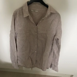 Beige linneskjorta från H&M - Säljer en stilren beige skjorta i linne från H&M. Skjortan har klassisk krage, knäppning framtill och långa ärmar. Perfekt för en avslappnad men ändå uppklädd look.