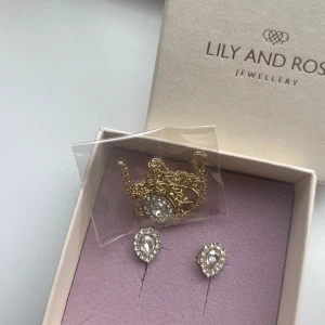 Lily and Rose Bianca örhängen och halsband  - Säljer ett set med Bianca örhängen och matchande halsband från Lily and Rose. Helt oanvända, påsen till halsbandet oöppnad. De är guldpläterade med droppformade klara kristaller omgivna av små gnistrande stenar. Nypris var 399kr/st men säljer nu hela setet för 100kr. 
