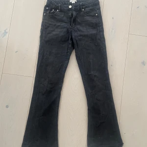 Svarta bootcut jeans medelhög midja - Säljer ett par svarta bootcut jeans med klassisk femficksdesign och knappgylf. Jeansen har en något utsvängd passform nertill och är tillverkade i ett stretchigt och skönt denimtyg. Jeansen har resårband i midjan. De är i storlek 158 från Gina Young.