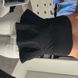 Svart peplum tubtopp - Säljer en svart peplum tubtopp med markerad midja och utsvängd nederdel. Toppen är axelbandslös och har en stilren look som passar till många olika outfits.
