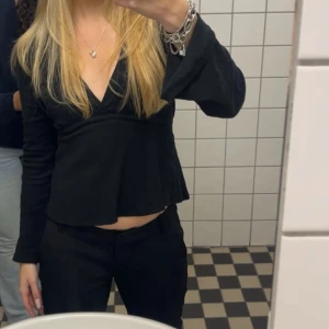 Svart topp med snörning - Säljer en svart topp med långa utsvängda ärmar och knytband i midjan. Toppen har v-ringning och är tillverkad i ett mjukt, ribbat material. Jättefint skick använd endast fåtal gånger. Nypris 300