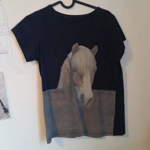 Svart t-shirt med hästmotiv från Copperfield - Svart t-shirt från Copperfield med ett stort tryck av en häst på framsidan. T-shirten har rund hals och korta ärmar. Perfekt för dig som gillar hästar och vill ha en unik t-shirt i garderoben.